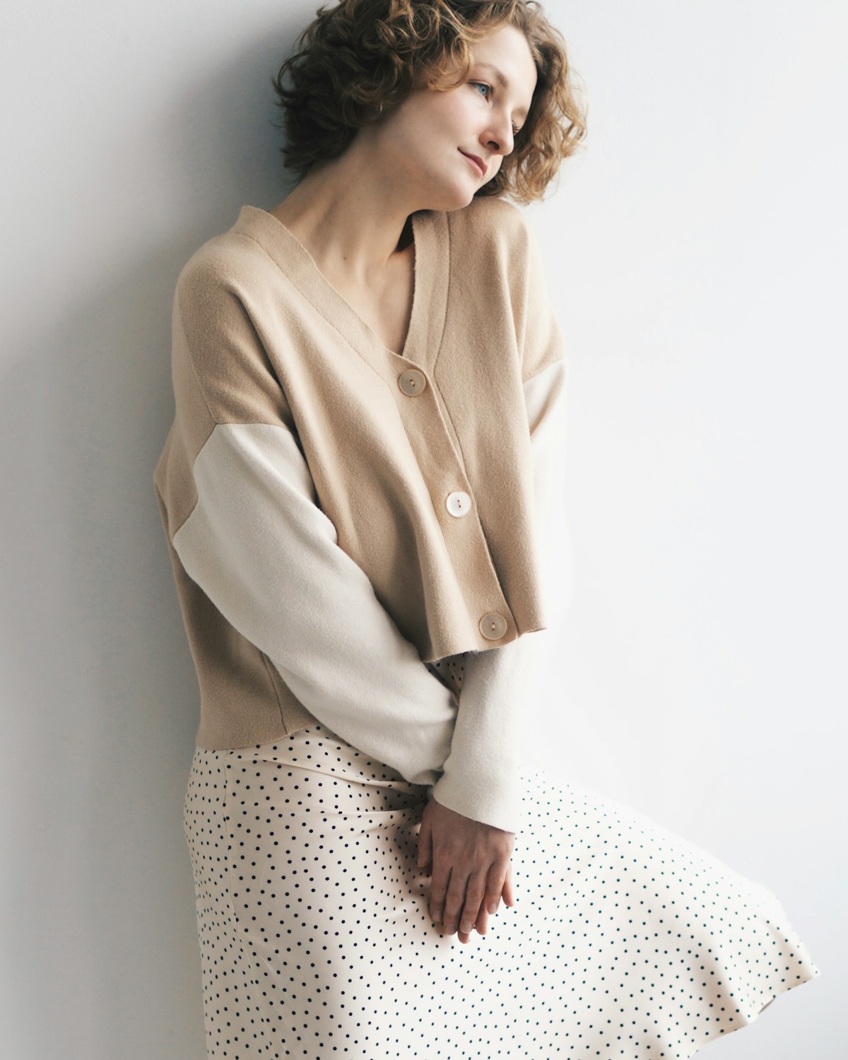 Woman in a sculptural neutral outfit against a simple wall